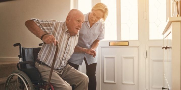 Photo of a nurse assisting an elderly man stand from his chair