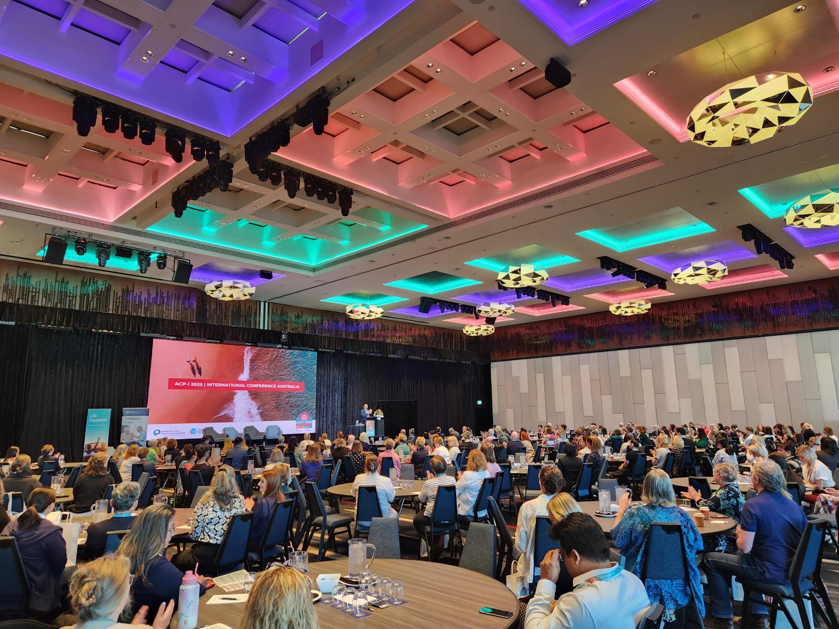Group of people in a large function space watching a big screen