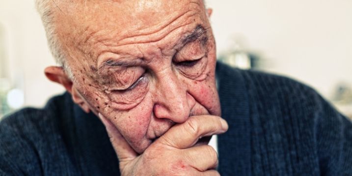 Elderly man with furrowed brow and hand on chin, appearing deep in thought.