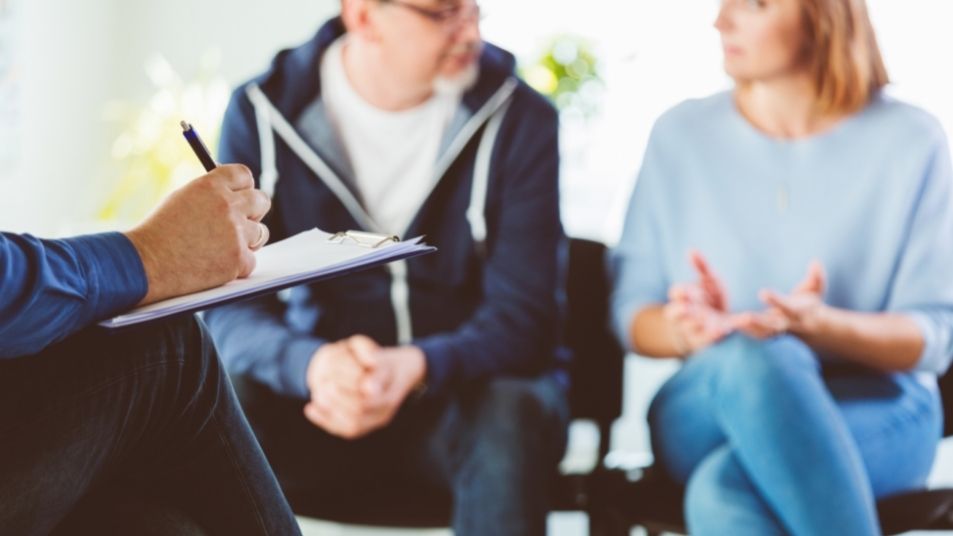 Close up photo of male hand writing on clipboard with couple out of focus in the background