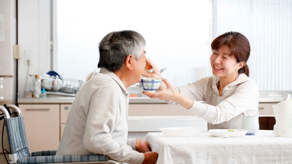 Photo of adult woman helping senior man eat a meal